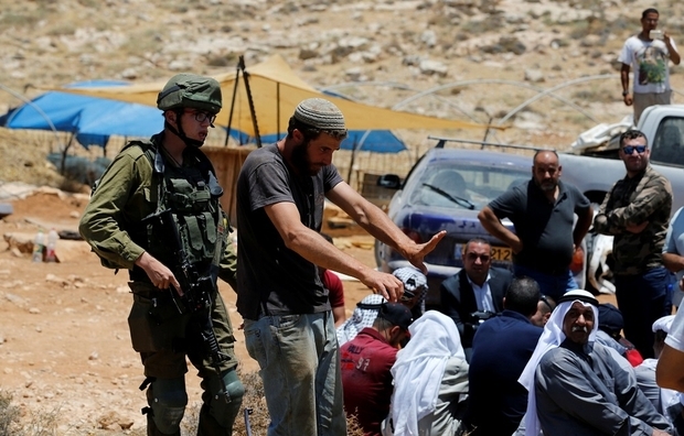 Un colon israélien protégé par un soldat fait des gestes en direction de Palestiniens qui protestent près d’Hébron en juin 2018 (Reuters)