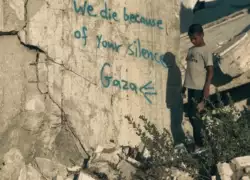 Un enfant devant un mur sur lequel est tagué - We die because of your silence - Gaza
